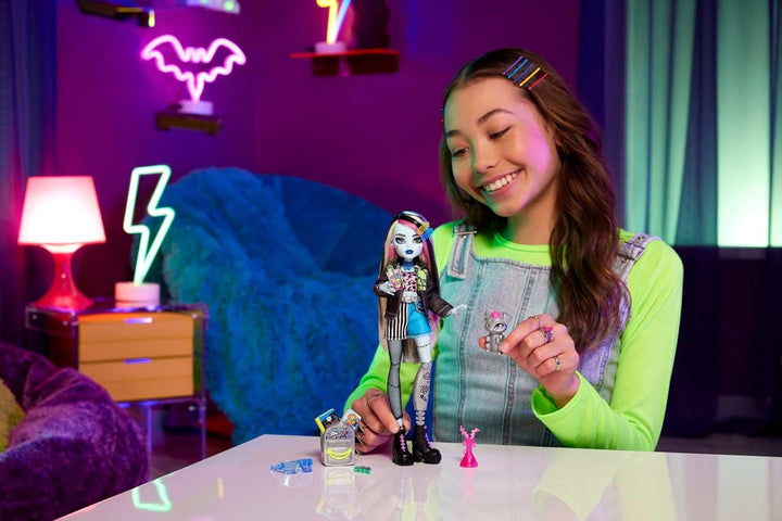 Păpușă Monster High Frankie Stone cu jachetă din denim și pantaloni scurți, include câinele Watzie și accesorii precum un rucsac, o gustare și un notebook, HXH73
